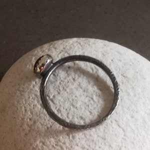 May include: A silver ring with a textured band and a round, silver bezel set with a small, red gemstone.