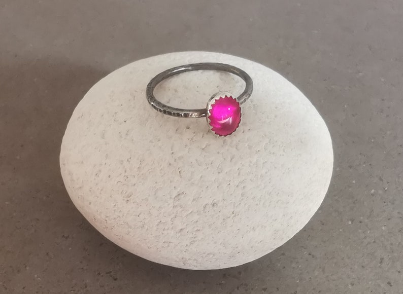 May include: A silver ring with a bright pink gemstone set in a textured silver bezel.