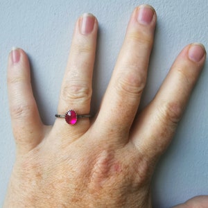 May include: A silver ring with a bright pink gemstone set in a bezel setting.