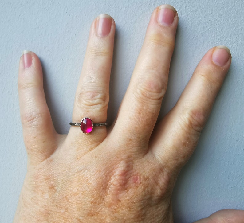 May include: A silver ring with a bright pink gemstone set in a bezel setting.