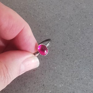 May include: A silver ring with a bright pink oval-shaped gemstone set in a silver bezel.