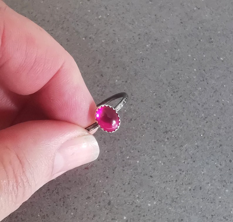 May include: A silver ring with a bright pink oval-shaped gemstone set in a silver bezel.