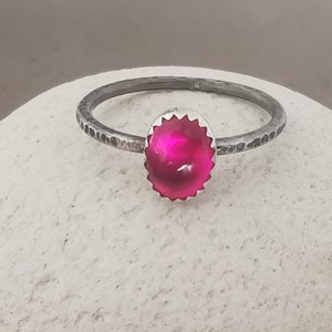 May include: A silver ring with a bright pink gemstone set in a textured silver bezel. The ring band is hammered and has a rustic look.