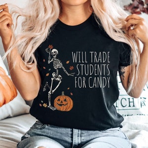 Pode incluir: Camiseta preta com um esqueleto segurando uma ab&oacute;bora e o texto "Will Trade Students For Candy".