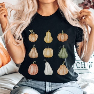 May include: Black t-shirt featuring a watercolor design of various pumpkins in shades of orange, yellow, and green. The pumpkins have different shapes and sizes, perfect for fall or autumn-themed apparel.