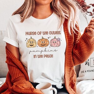 May include: White t-shirt with the text "Nurse of the cutest pumpkins in the patch" and three cartoon pumpkins with different facial expressions.