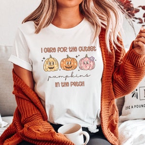 May include: White t-shirt with a graphic of three cartoon pumpkins and the text "I care for the cutest pumpkins in the patch".