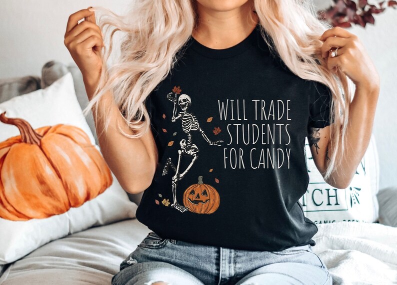 Pode incluir: Camiseta preta com um esqueleto segurando uma ab&oacute;bora e o texto "Will Trade Students For Candy".