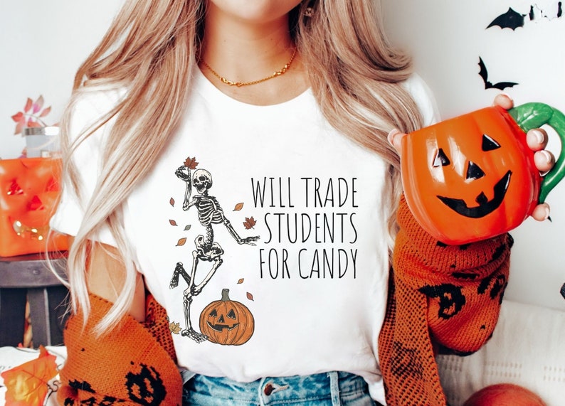Pode incluir: Camiseta branca com um esqueleto segurando uma folha e uma ab&oacute;bora. O texto na camiseta diz "Will Trade Students For Candy".
