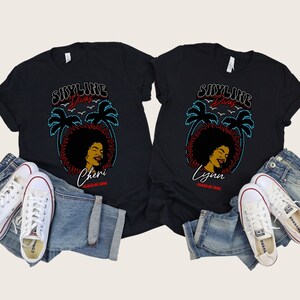 May include: Two black t-shirts with a retro design featuring palm trees, a woman with an afro, and the text "Skyline Divas". The shirts have the names "Cheri" and "Lynn" and the text "Class of 2022" printed on them.