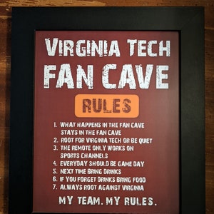 May include: A framed print with a red background and white text that reads "Virginia Tech Fan Cave Rules". The rules are listed below the title, including "What happens in the fan cave stays in the fan cave" and "Always root against Virginia".