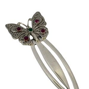 May include: Silver butterfly bookmark with pink and green gemstones. The bookmark is shaped like a butterfly with intricate details and a long, thin, silver bookmark attached to the bottom.