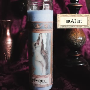 Pode incluir: Uma vela de vidro cilíndrica alta preenchida com cera azul clara. O rótulo apresenta uma pintura clássica de uma figura e o texto Aphrodite of the sea. Uma placa retangular com borda decorativa exibe o texto no AI art em preto.