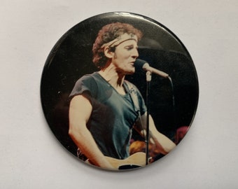 May include: A black and white photo of a musician singing into a microphone while holding a guitar. The musician is wearing a black t-shirt and a headband.