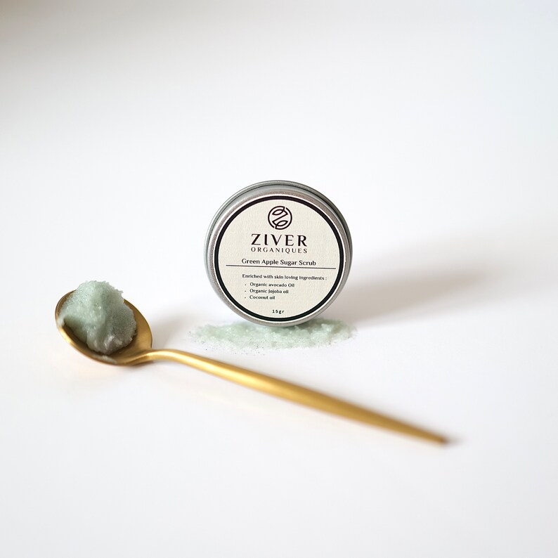 Puede incluir: Una lata plateada con un exfoliante de az&uacute;car de manzana verde en su interior. La lata tiene una etiqueta negra con el texto "Ziver Organiques" y "Green Apple Sugar Scrub". El exfoliante tambi&eacute;n se muestra en una cuchara dorada.