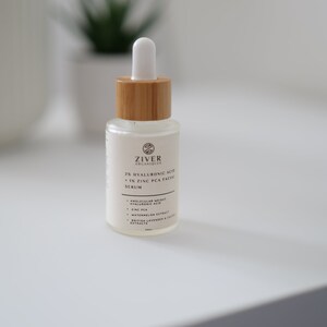 May include: A clear glass bottle with a wooden cap and a dropper top. The bottle is labeled "Ziver Organiques 2% Hyaluronic Acid + 1% Zinc PCA Facial Serum". The label also lists the ingredients: "Molecular Weight Hyaluronic Acid, Zinc PCA, Watermelon Extract, British Lavender & Chamomile Extracts".