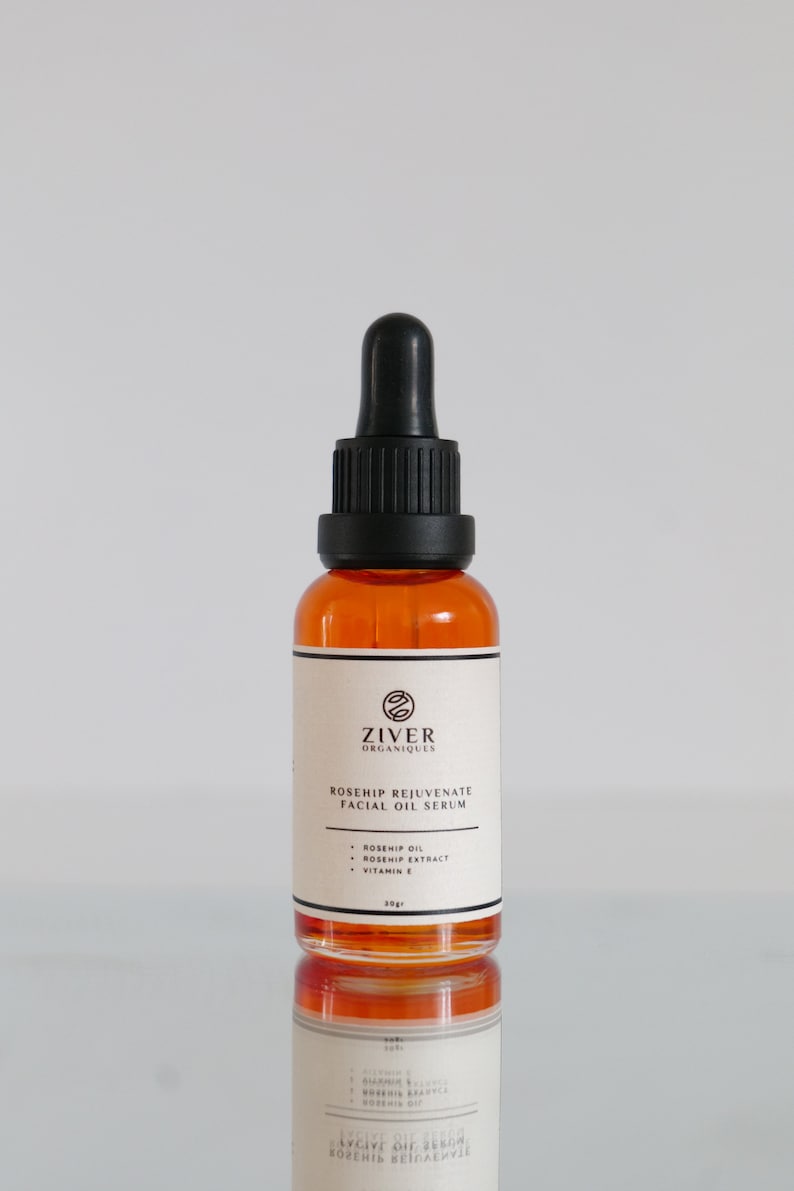 May include: A clear glass bottle with a black dropper top filled with a light orange liquid. The bottle is labeled "ZIVER ORGANIQUES ROSEHIP REJUVENATE FACIAL OIL SERUM" and lists the ingredients as "ROSEHIP OIL, ROSEHIP EXTRACT, VITAMIN E". The bottle contains 30 grams of product.