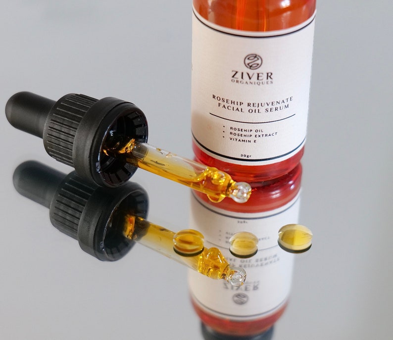 May include: A glass bottle of rosehip facial oil serum with a dropper. The bottle is labeled "Ziver Organiques Rosehip Rejuvenate Facial Oil Serum" and lists the ingredients as rosehip oil, rosehip extract, and vitamin E.
