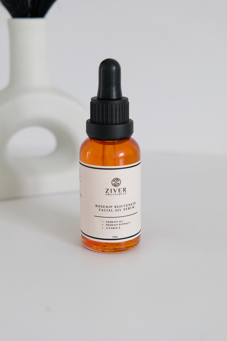 May include: A clear glass bottle with a black dropper top filled with a yellow liquid. The bottle is labeled "Ziver Organiques Rosehip Rejuvenate Facial Oil Serum" and lists the ingredients as "Rosehip Oil, Rosehip Extract, Vitamin E". The bottle is 30 ml.