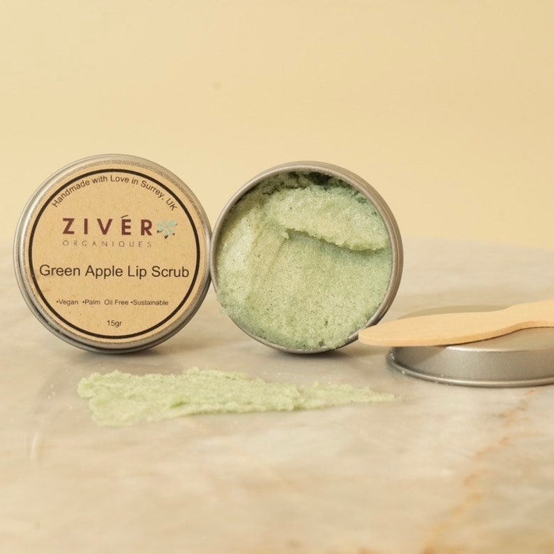 Puede incluir: Un peque&ntilde;o bote de exfoliante labial de manzana verde con una esp&aacute;tula de madera. El bote est&aacute; etiquetado con "ZIVER ORGANIQUES Exfoliante labial de manzana verde Vegano Libre de aceite de palma Sostenible 15gr".