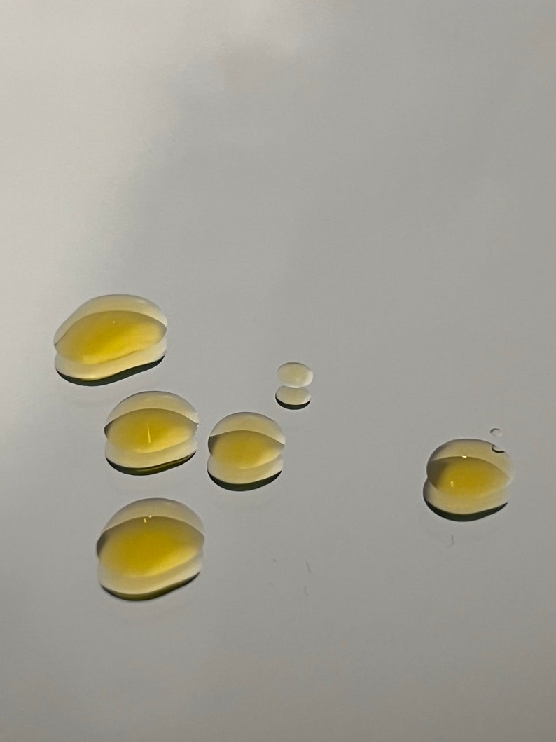 May include: Six drops of a clear, yellow liquid on a white surface.
