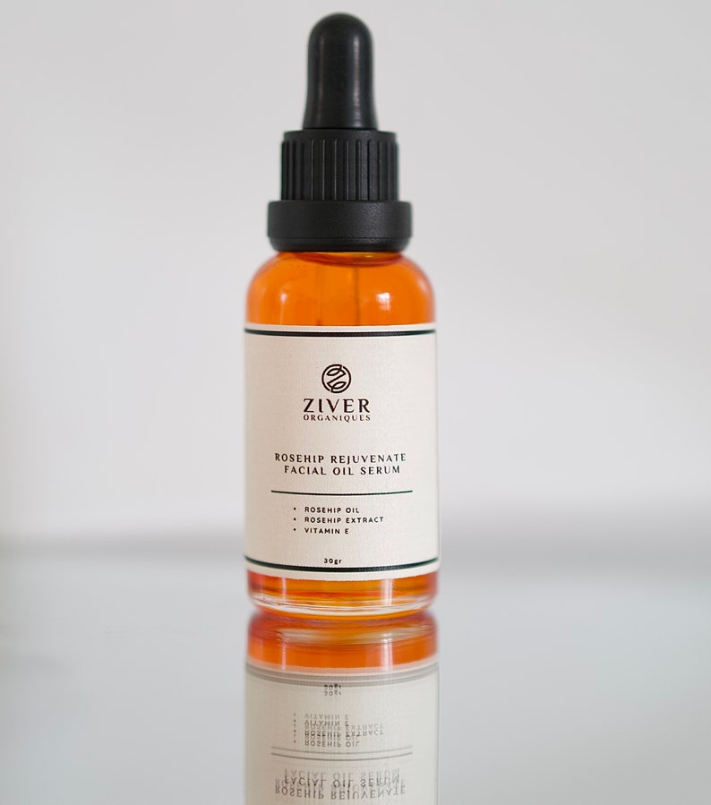 May include: A 30-gram amber glass bottle of rosehip rejuvenate facial oil serum with a black dropper top. The label is white with black text that reads "Ziver Organiques Rosehip Rejuvenate Facial Oil Serum" and lists the ingredients: "Rosehip Oil, Rosehip Extract, Vitamin E".