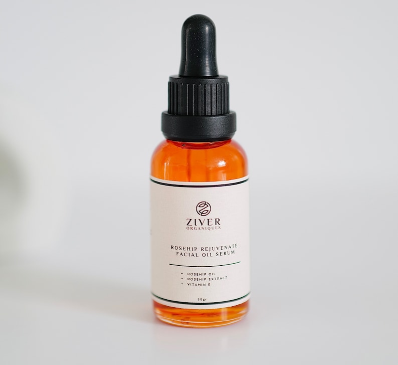 May include: A glass bottle of rosehip facial oil serum with a black dropper. The bottle is labeled "Ziver Organiques Rosehip Rejuvenate Facial Oil Serum" and lists the ingredients as rosehip oil, rosehip extract, and vitamin E. The bottle is 30 ml.