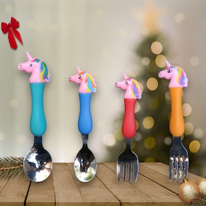 May include: Four colorful unicorn-shaped children's utensils, including a spoon and fork, with rainbow accents. The utensils are made of stainless steel and have plastic handles.