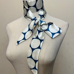 May include: A white silk scarf with large blue polka dots tied around a mannequin's neck.