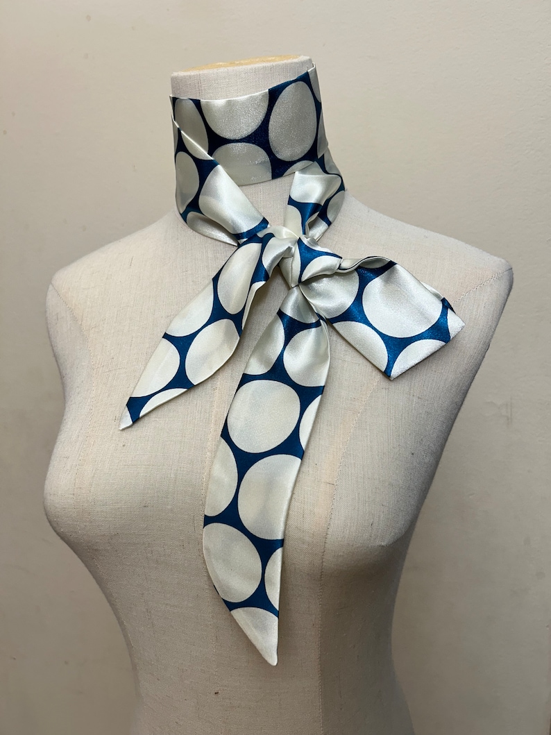 May include: A white silk scarf with large blue polka dots tied around a mannequin's neck.