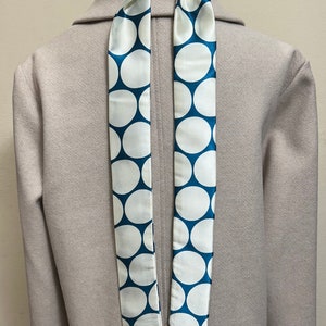 May include: A white coat with a blue and white polka dot scarf tied around the neck.