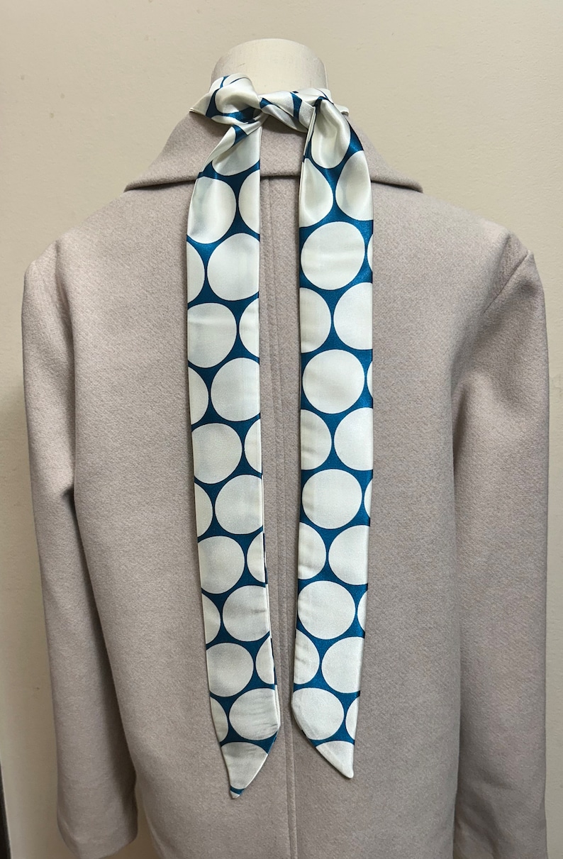 May include: A white coat with a blue and white polka dot scarf tied around the neck.
