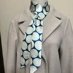May include: A white and teal blue polka dot patterned scarf tied around a mannequin's neck.