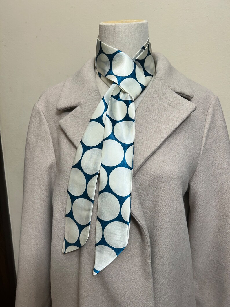May include: A white and teal blue polka dot patterned scarf tied around a mannequin's neck.