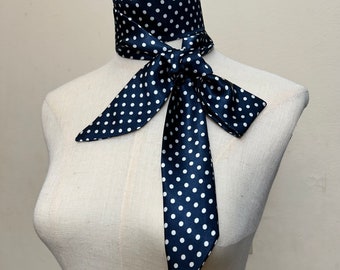 May include: A navy blue satin scarf with white polka dots tied in a bow around a white mannequin's neck.