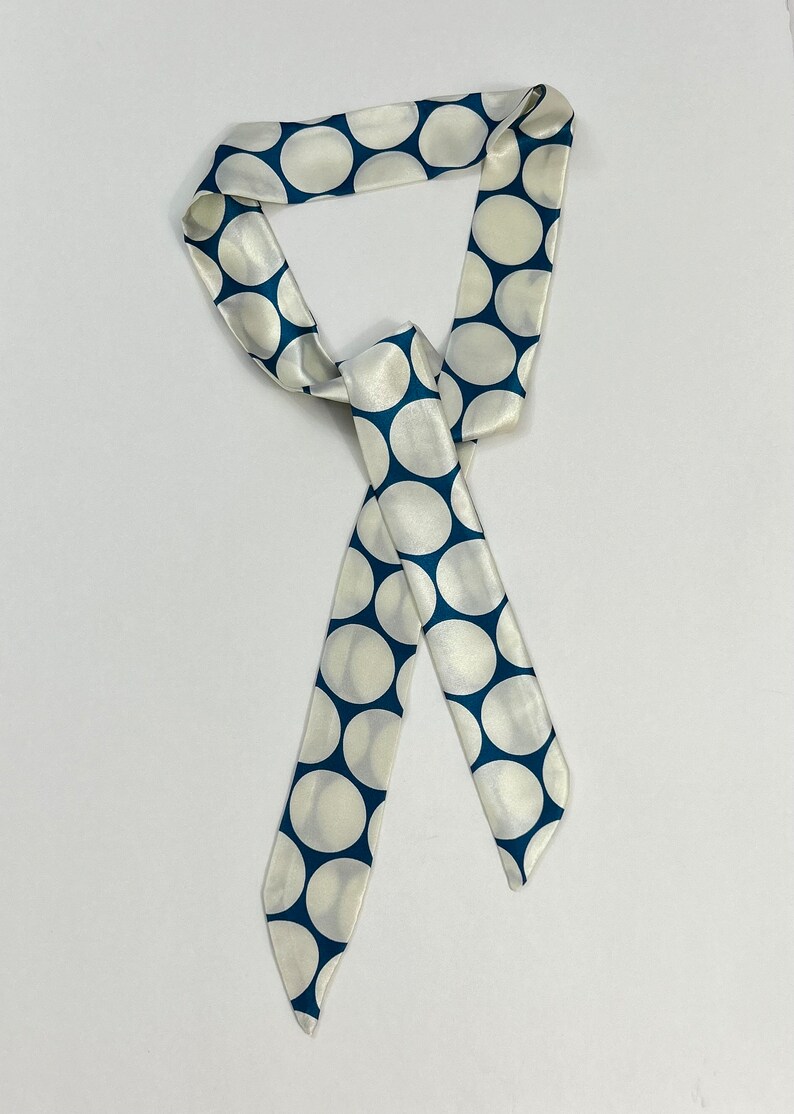May include: A white satin scarf with a blue polka dot pattern. The scarf is tied in a loose knot.