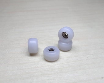 May include: Four white fingerboard wheels with black bearings. The wheels are stacked on top of each other.