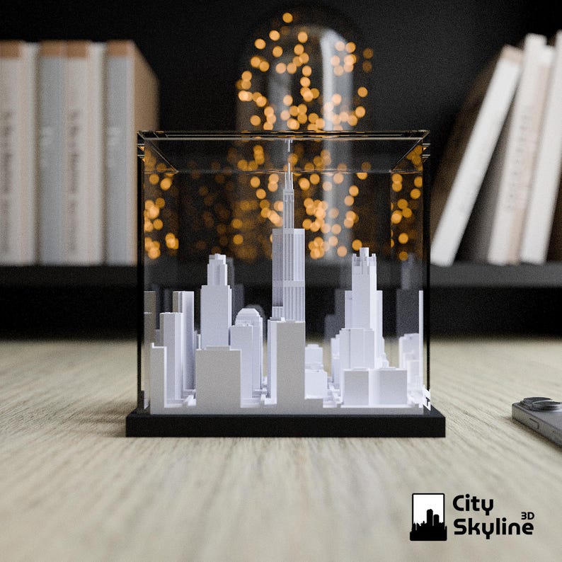 Puede incluir: Maqueta 3D blanca de un horizonte urbano, encerrada en una caja de acr&iacute;lico transparente con base negra. El modelo presenta edificios de diversas formas. El logotipo City Skyline 3D est&aacute; en la esquina inferior derecha.
