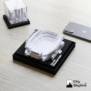 May include: A white 3D model of Lincoln Financial Field stadium on a black base. The model is detailed with seating sections and architectural features. The text "Lincoln Financial Field" is printed on the base. A second model of a city skyline is in the background.