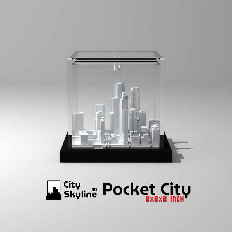 Puede incluir: Un modelo 3D de un horizonte urbano blanco, presentado en una vitrina de acr&iacute;lico transparente. El modelo est&aacute; sobre una base negra. La vitrina est&aacute; etiquetada como "Pocket City 2x2x2 INCH", que son aproximadamente 5 x 5 x 5 cm.