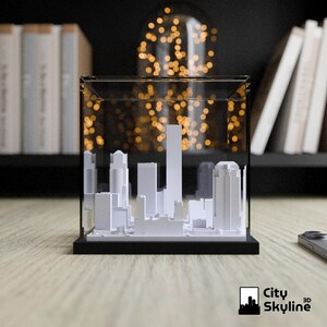 May include: A white 3D city skyline model inside a clear display case with a black base. The model features various building shapes and sizes. The City Skyline 3D logo is in the bottom right corner.