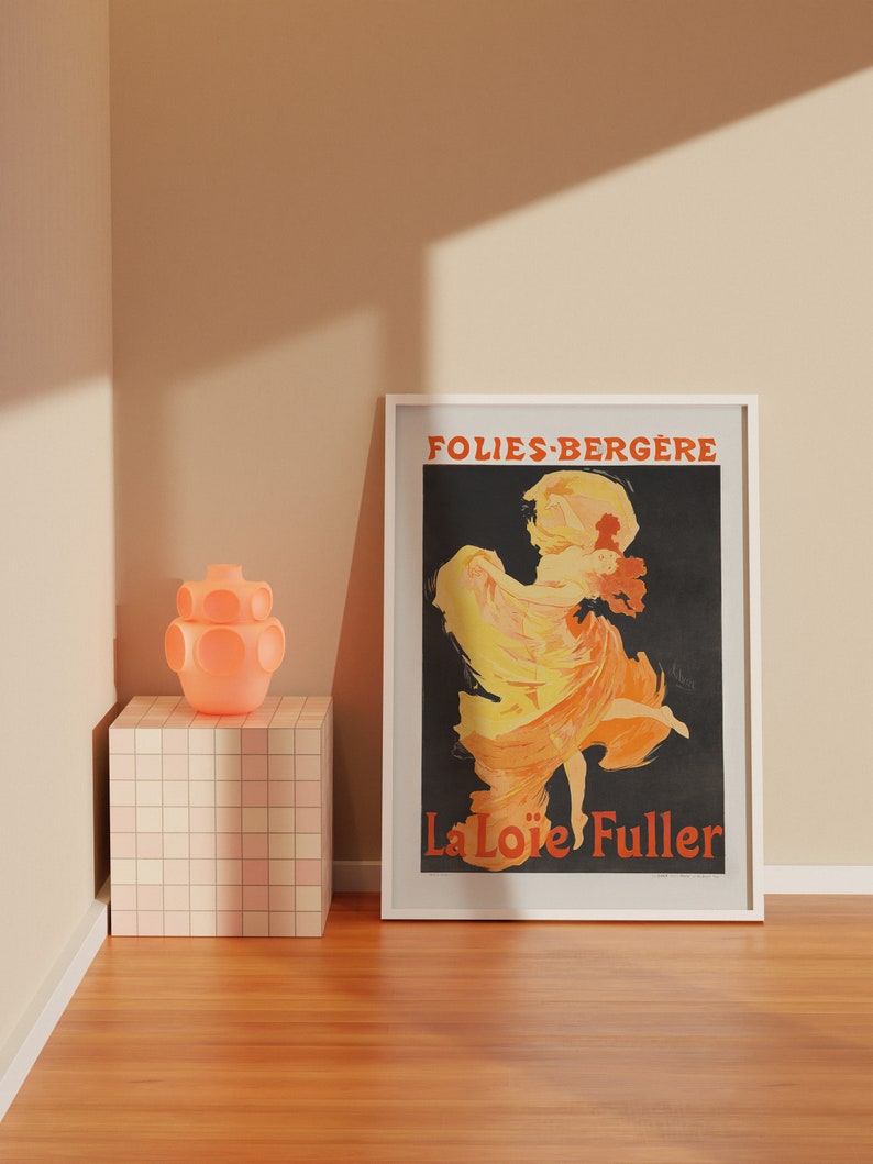 May include: A white framed poster with a black background featuring a woman in a yellow and orange dress dancing. The text "Folies-Berg&egrave;re" and "La Lo&iuml;e Fuller" is printed in red on the poster.