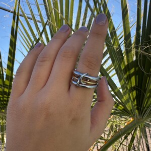 May include: A silver and gold ring with a twisted design. The ring is worn on a finger.