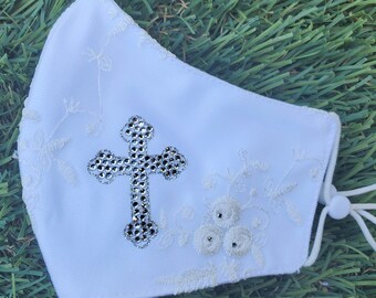 May include: White face mask with a white embroidered floral design and a silver rhinestone cross in the center.