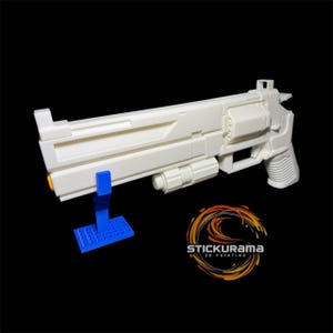 Könnte beinhalten: Eine weiße 3D-gedruckte Requisitenpistole mit futuristischem Design, mit langem Lauf und detailliertem Griff. Die Waffe wird von einem blauen Ständer getragen. Das Logo "STICKURAMA 3D PRINTING" ist unten rechts sichtbar.
