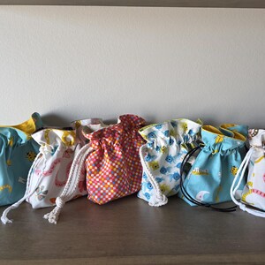May include: A collection of drawstring pouches in various patterns and colors. The pouches feature designs such as butterflies, flowers, and geometric patterns. Each pouch has a contrasting interior and a drawstring closure.