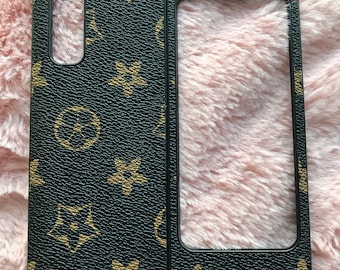 May include: A black phone case with a brown and gold pattern. The case has a cutout for the camera lens and a clear window on the back.