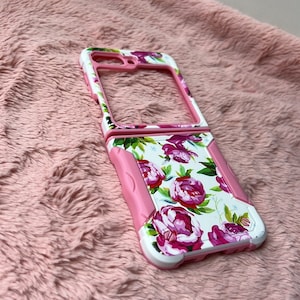 Puede incluir: Una funda para teléfono rosa y blanca con un diseño floral con grandes peonías rosas y hojas verdes. La funda tiene un diseño protector y resistente con protector de pantalla integrado y soporte.