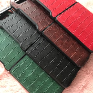 May include: A collection of phone cases in various colors, including red, brown, black, and green. Each case features a textured, crocodile-like pattern and a black border, offering a stylish and protective design for smartphones.