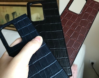 Puede incluir: Tres fundas para teléfono con un diseño de cuero estampado de cocodrilo. Las fundas son negras, azul oscuro y marrón.